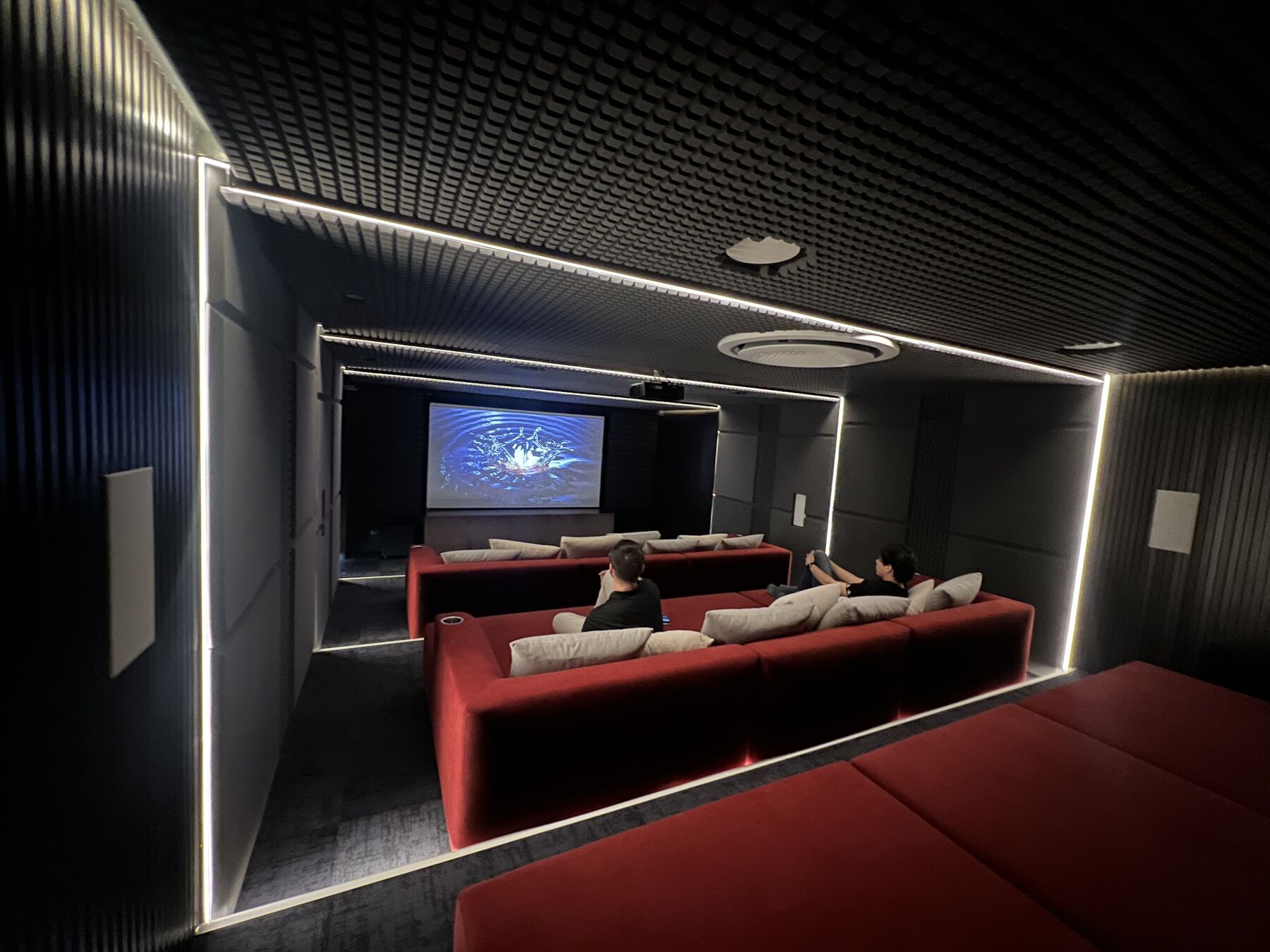 Sala de cine en casa con pantalla, butacas rojas y acústica diseñada por Biosystem Technology