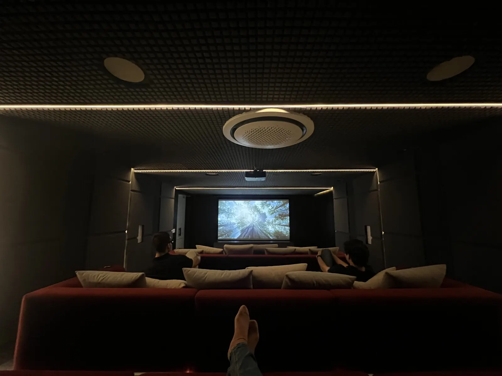 Cine privado en funcionamiento con proyector, butacas rojas y acústica tratada